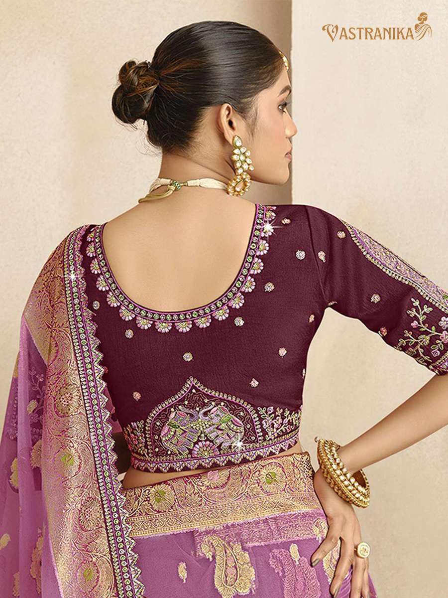 Woman wearing a purple embroidered saree with gold details, branded 'Vastranika'.