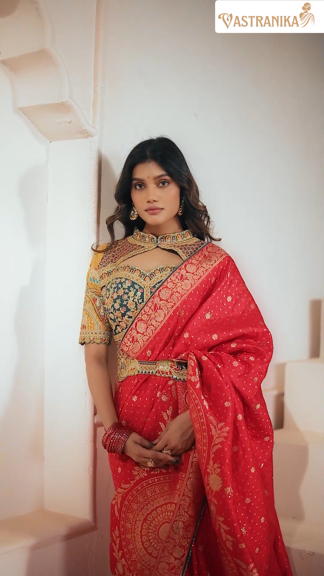 Woman wearing a red saree with gold patterns, standing indoors.