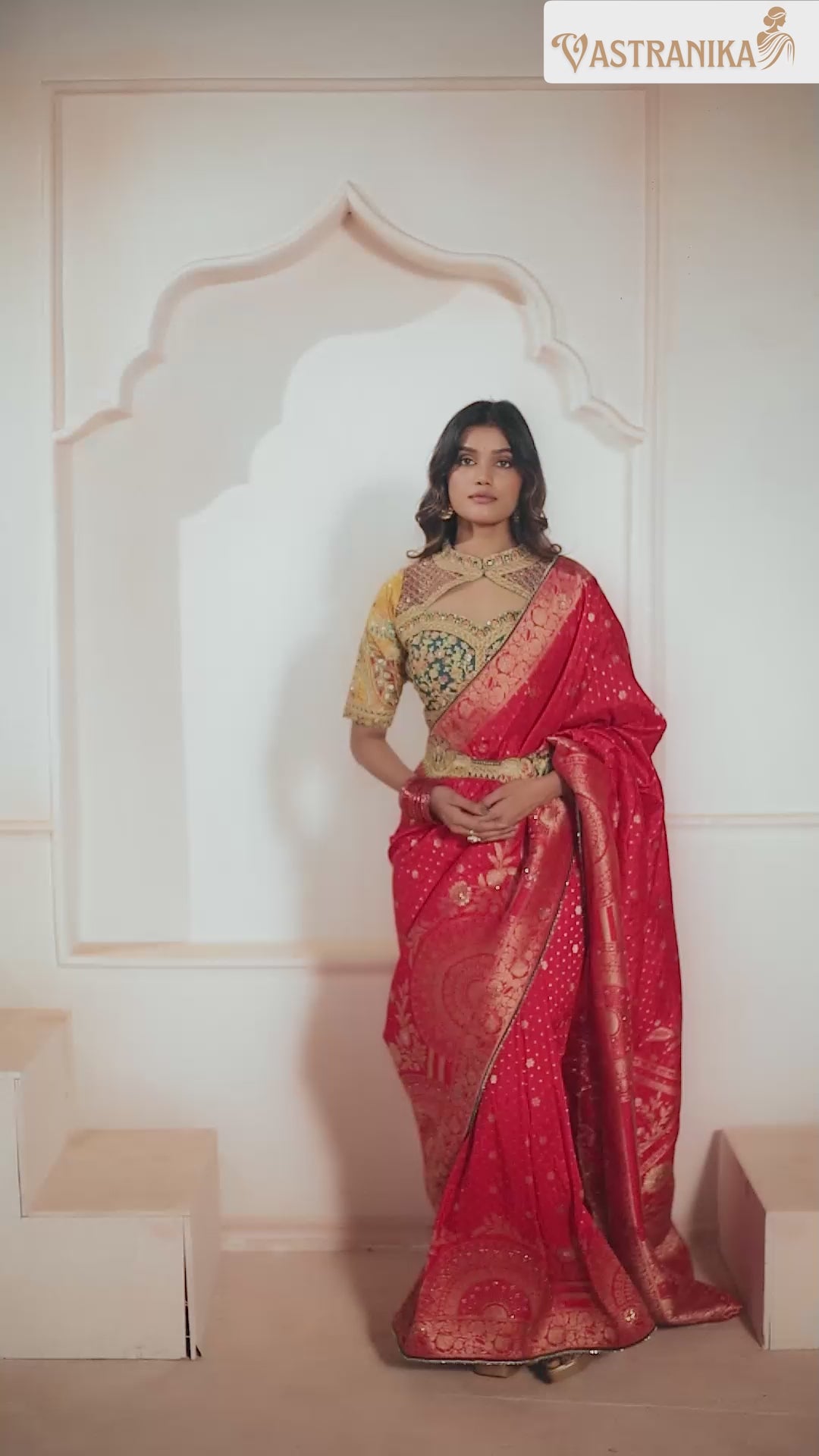 Model wearing red premium silk saree with rich golden motifs and grand pallu, styled with a contrast designer blouse – shot against a white wall, from Vastranika's Weaves collection.

